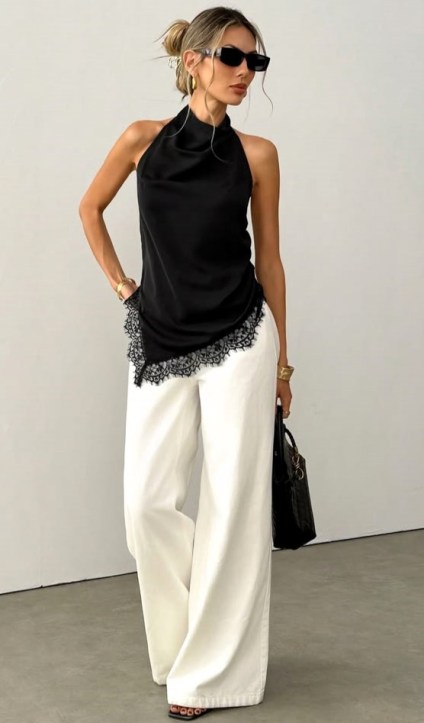 Mulher em um top preto com detalhes de rendas, usando calças largas brancas e óculos escuros, posando em um ambiente minimalista.