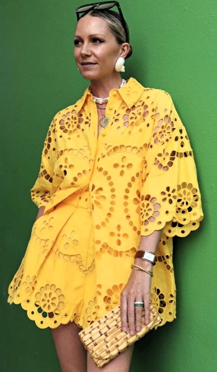 Mulher vestindo um conjunto amarelo brilhante com recortes florais, posando contra uma parede verde.