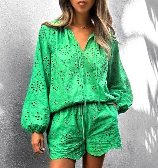 Mulher usando um conjunto verde com blusa de mangas bufantes e shorts, decorado com detalhes em rendado.