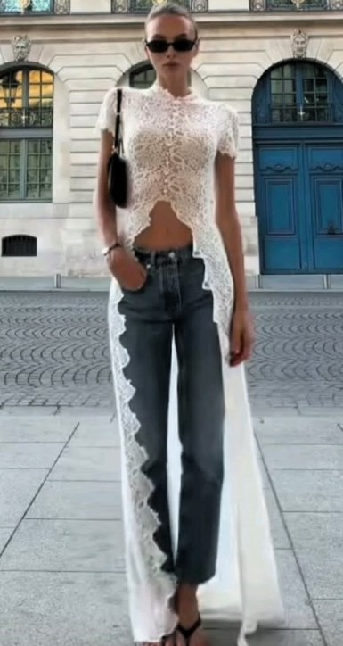Modelo usando uma blusa de renda branca e jeans, posando na rua com óculos escuros.